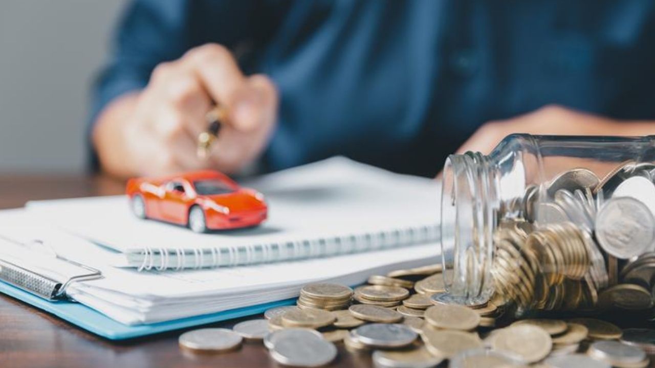 Man writing on notebook with a red mini car on top of it and a jar of coins tumbled on the table