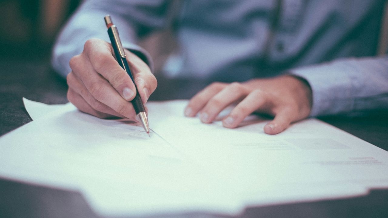 Man wearing a blue shirt signing a contract on the table