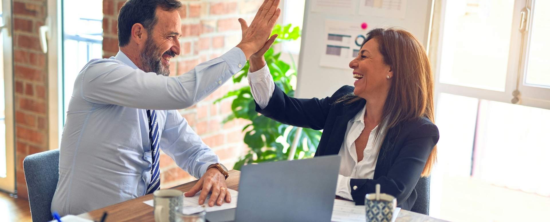 Man in shirt and tie high-fiving a woman wearing a blazer and white shirt