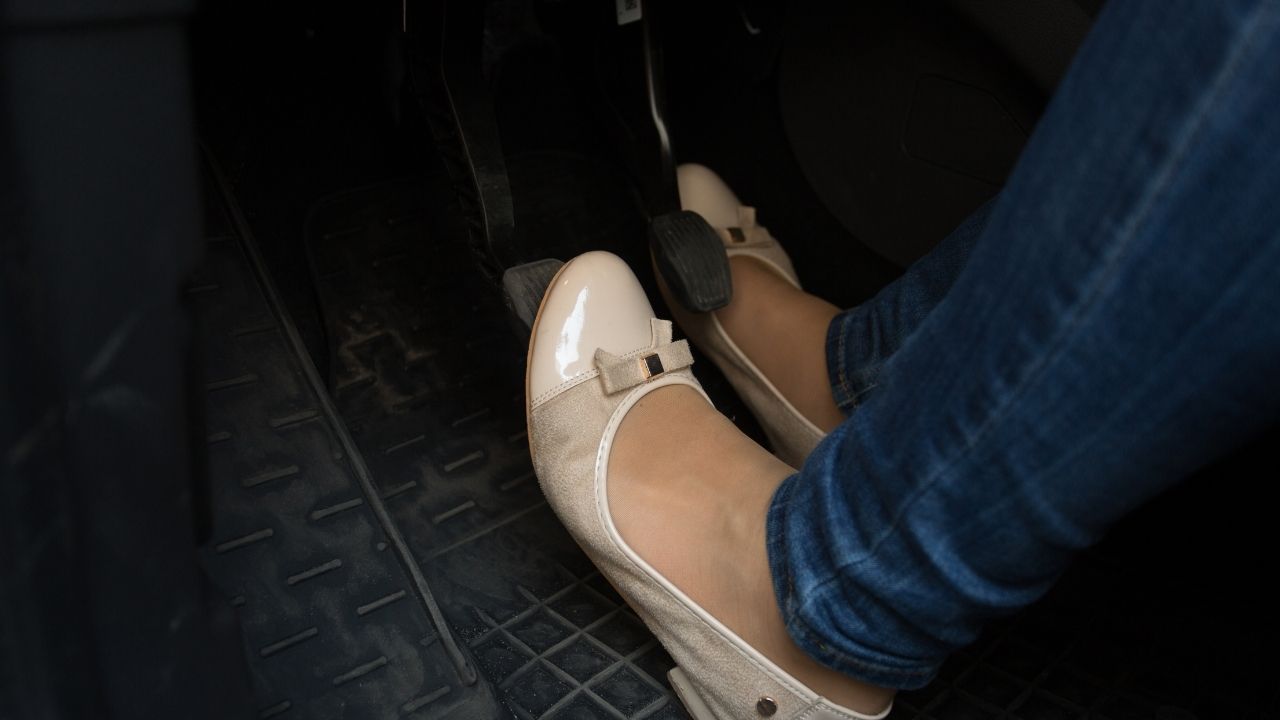 Woman wearing beige flats stepping on a car pedal