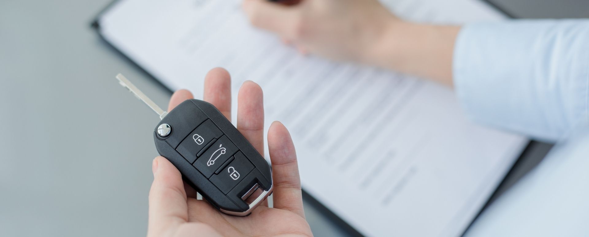 Man holding a car key on his left hand and signing a contract with his right hand