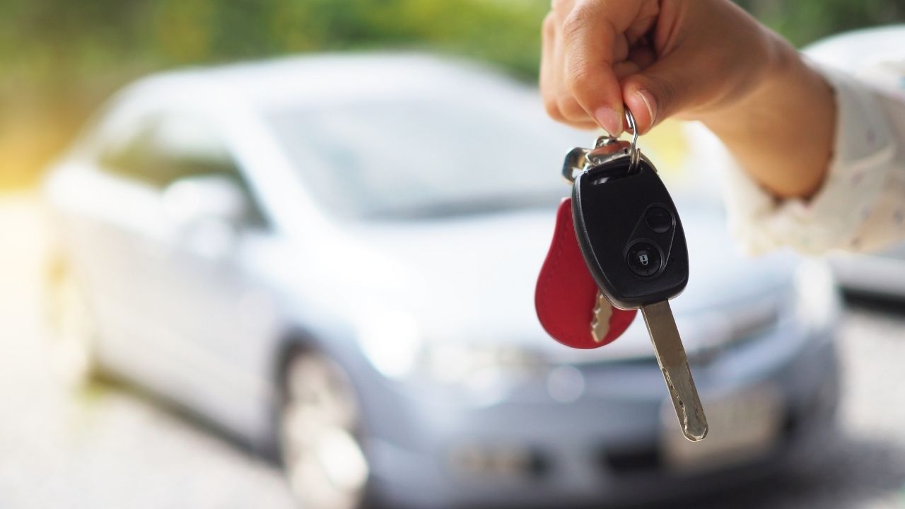 Woman holding car keys in front of a blurry car in the background