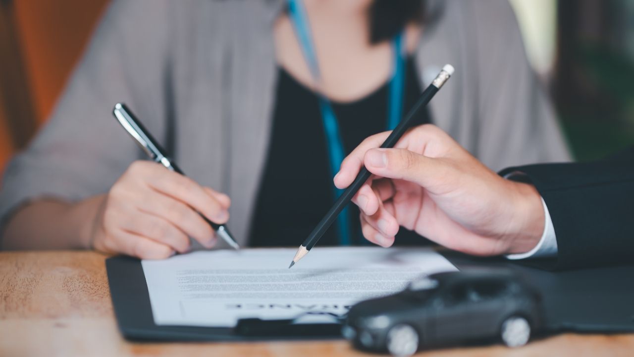 Woman holding a pen and signing a contract whilst a man is holding a pencil and pointing to a specific paragraph